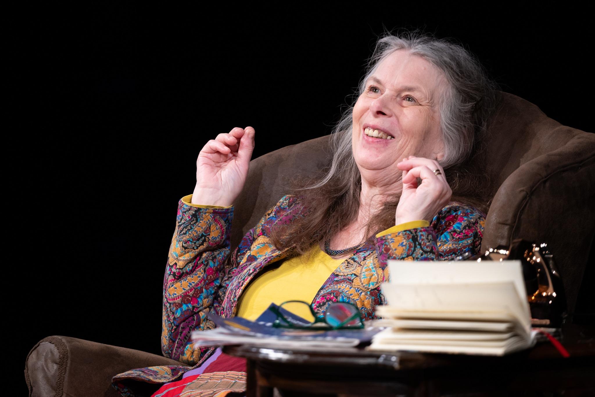 Woman leaning back in an armchair, sat beside a book and a dial-up telephone.
